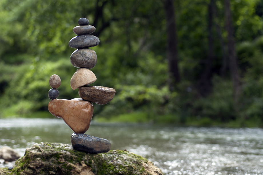 Steinskulptur aus balancierten Kieselsteinen am Flussufer mit Wald im Hintergrund