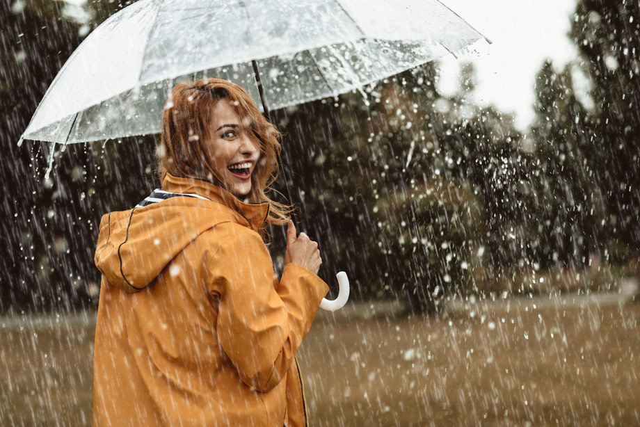 Lachende Frau im strömenden Regen mit einem transparenten Regenschirm